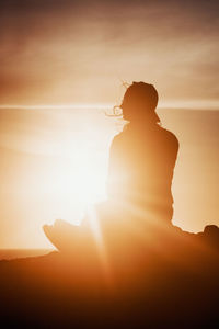 Silhouette man standing on rock against sky during sunset