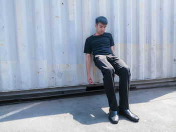 Full length of man sitting against wall