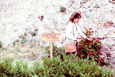 Side view of woman looking at flowers by wall