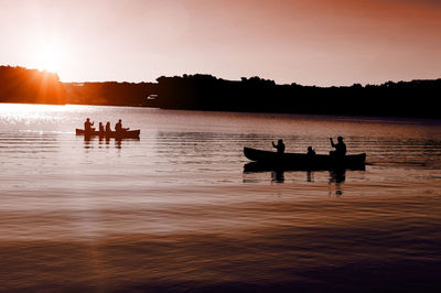 Silhouette people sitting on lake against sky during sunset