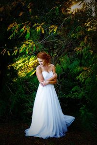Bride standing in wedding dress against trees