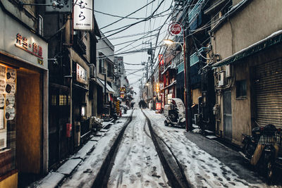 Snowy road amidst buildings in city