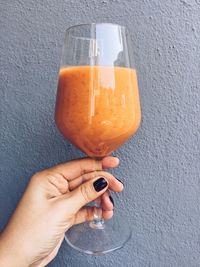 Cropped hand of woman holding drink in wineglass by wall