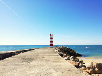 Lighthouse on beach against clear blue sky