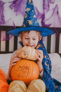 Little preschooler boy in festive halloween costume with a pumpkin lantern jack at home