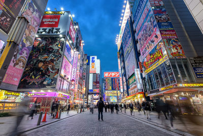 People walking on illuminated street amidst buildings in city