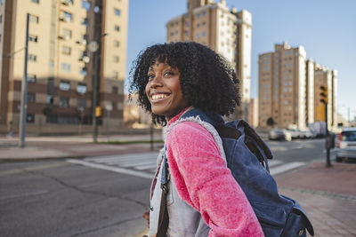 Happy young woman with backpack standing on footpath