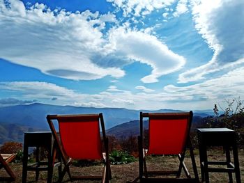 Empty chairs on landscape against sky
