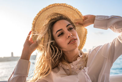 Close-up of beautiful woman wearing hat standing at beach against sky