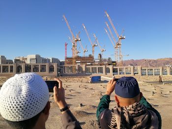 Rear view of people at construction site against clear blue sky