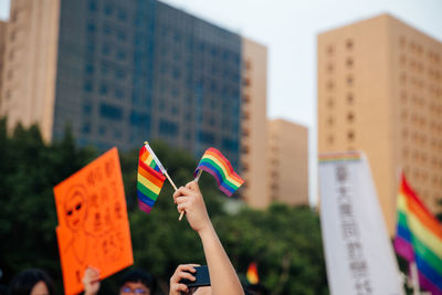 Cropped hand holding rainbow flags against buildings