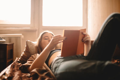 Teenage girl reading book while lying on bed at home