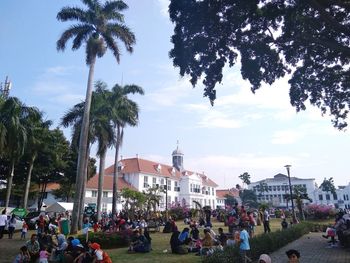 People on street by palm trees and buildings against sky