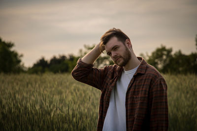 Young man looking away on field against sky during sunset