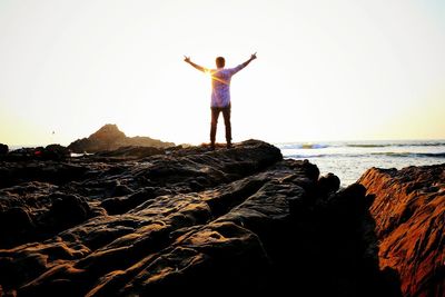 Rear view of young woman standing on beach against clear sky