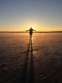 Silhouette man standing on beach against sky during sunset