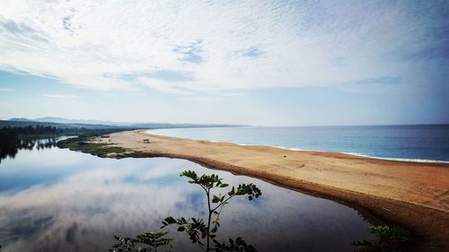 View of calm beach against cloudy sky