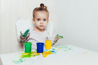 Portrait of cute girl with messy hands sitting on chair against wall at home