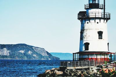 Lighthouse by sea against clear sky