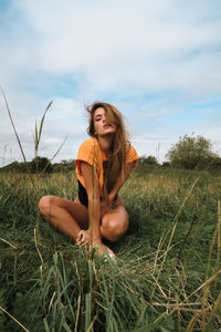 Woman with long hair wearing orange top siting in a green field