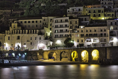 Arch bridge over river by buildings in atrani, amalfi coast, at night 