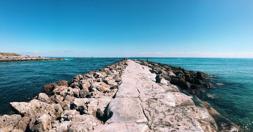 Groyne in sea against blue sky