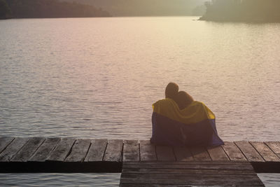 Rear view of woman sitting on pier over sea against sky