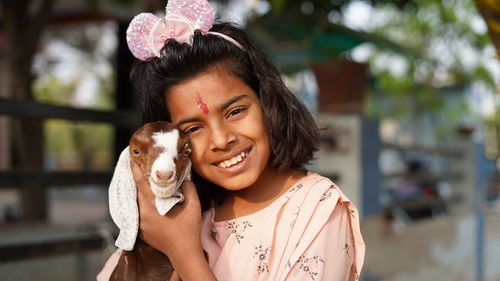 A baby goat being held by a shy little indian girl aged 10 years old peeping out from behind it.