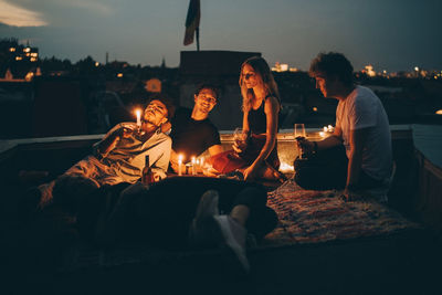 Friends enjoying wine in candlelight while relaxing on terrace at city during dusk