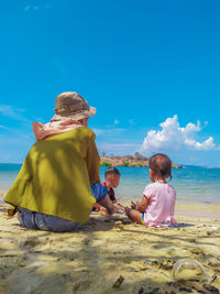 Rear view of woman sitting at beach against clear blue sky