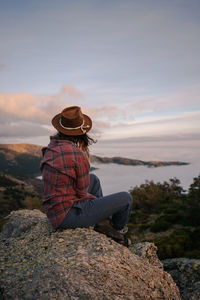 Man sitting on rock looking at mountains against sky