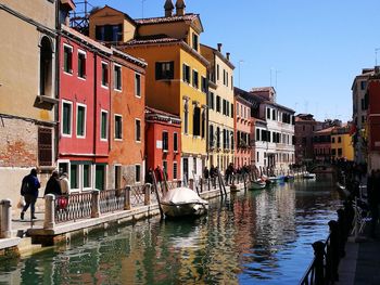 People on canal by buildings in city