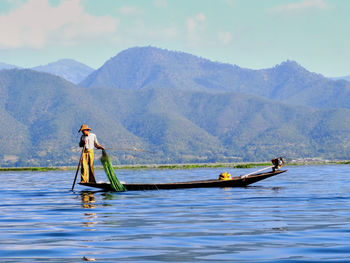 Fisherman standing on boat in sea against mountains