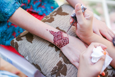 Cropped image of beautician making henna tattoo on woman hand