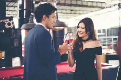 Smiling couple toasting red wineglasses while standing in bar