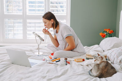 Woman doing make up while sitting on bed at home