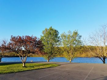 Road by lake against clear blue sky