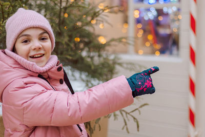 Little happy girl in pink at christmas fair. people buy gifts for holiday at christmas market