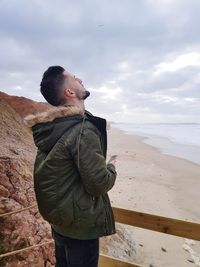 Man standing by railing at beach against sky