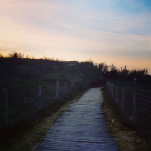 Footpath by railing against sky during sunset