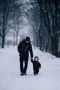 Father holding baby daughter hand while walking on snow covered land