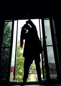 Low angle view of silhouette man standing against window at home