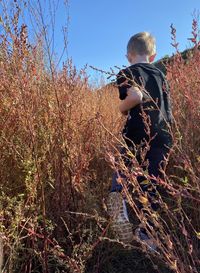 Little boy following an overgrown trail with tall grasses autumn colors