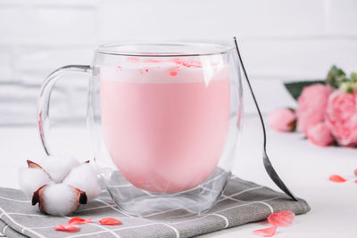 Pink matcha with rose petals on a white background. transparent cup with trendy vegan whipped tea.