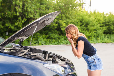 Woman sitting on car against trees