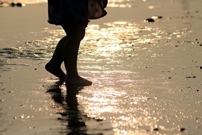 Low section of woman standing on wet shore during sunset