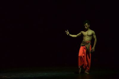 Shirtless young man performing on stage in dark