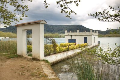 House by lake and buildings against sky