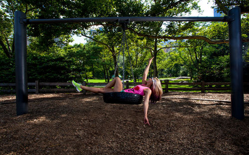 Side view full length of woman relaxing on swing at park