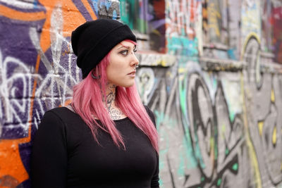 Young woman in pink hair standing against graffiti wall